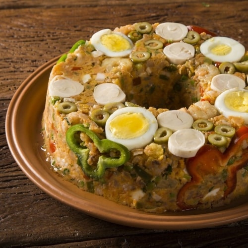 Cuscuz paulista servido em refratário redondo, com ovo cozido, pimentão e azeitonas aparentes