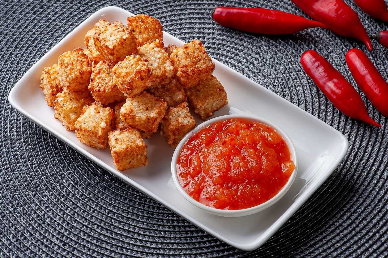 Dadinhos de tapioca, bem servidos, ao lado de pote de geleia de pimenta