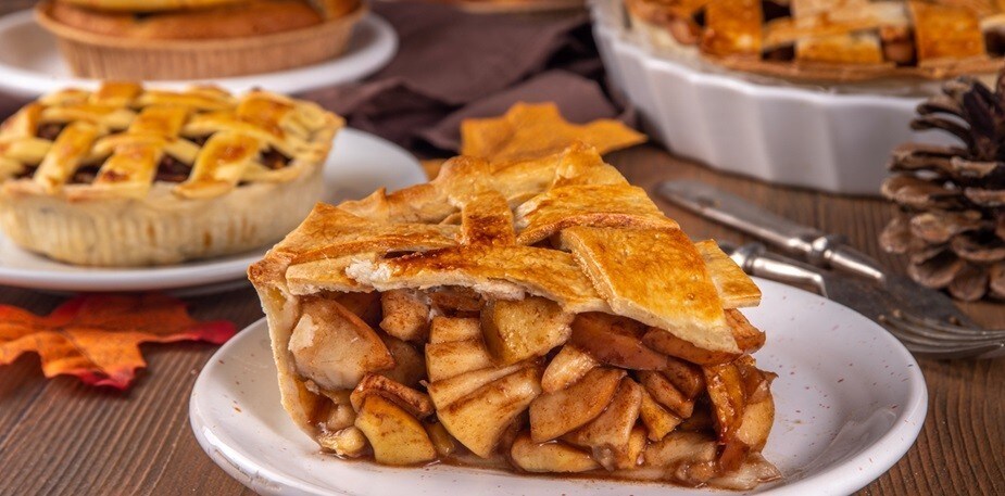 Fatia de torta de maçã sobre um prato, com tortas ao fundo. Fatia de torta de maçã sobre um prato, com tortas ao fundo.