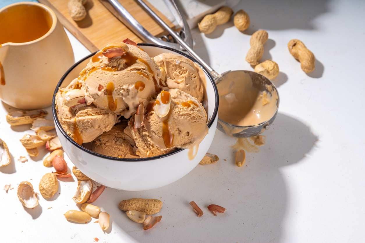 Sorvete de amendoim servido em cumbuca branca, com calda de caramelo e amendoim sem pele