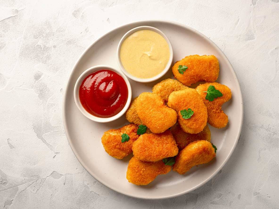 Prato com nuggets de frango caseiros, potinho de ketchup e um outro com maionese.