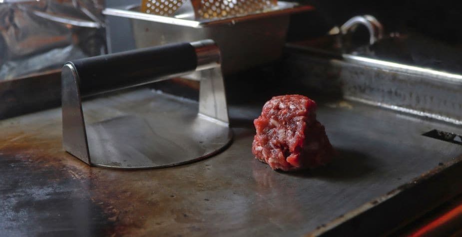 Chapa quente, com uma bola de carne moída preparada para se tornar um suculento hambúrguer. Chapa quente, com uma bola de carne moída preparada para se tornar um suculento hambúrguer.