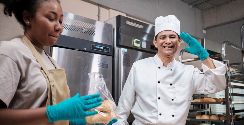 Profissionais de padaria felizes e fazendo sinal de joia, após separar pães de fornada para cliente Profissionais de padaria felizes e fazendo sinal de joia, após separar pães de fornada para cliente