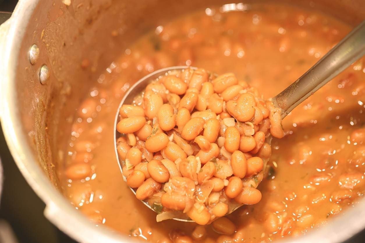 Feijão cozido, coletado por concha, ainda na panela de pressão.