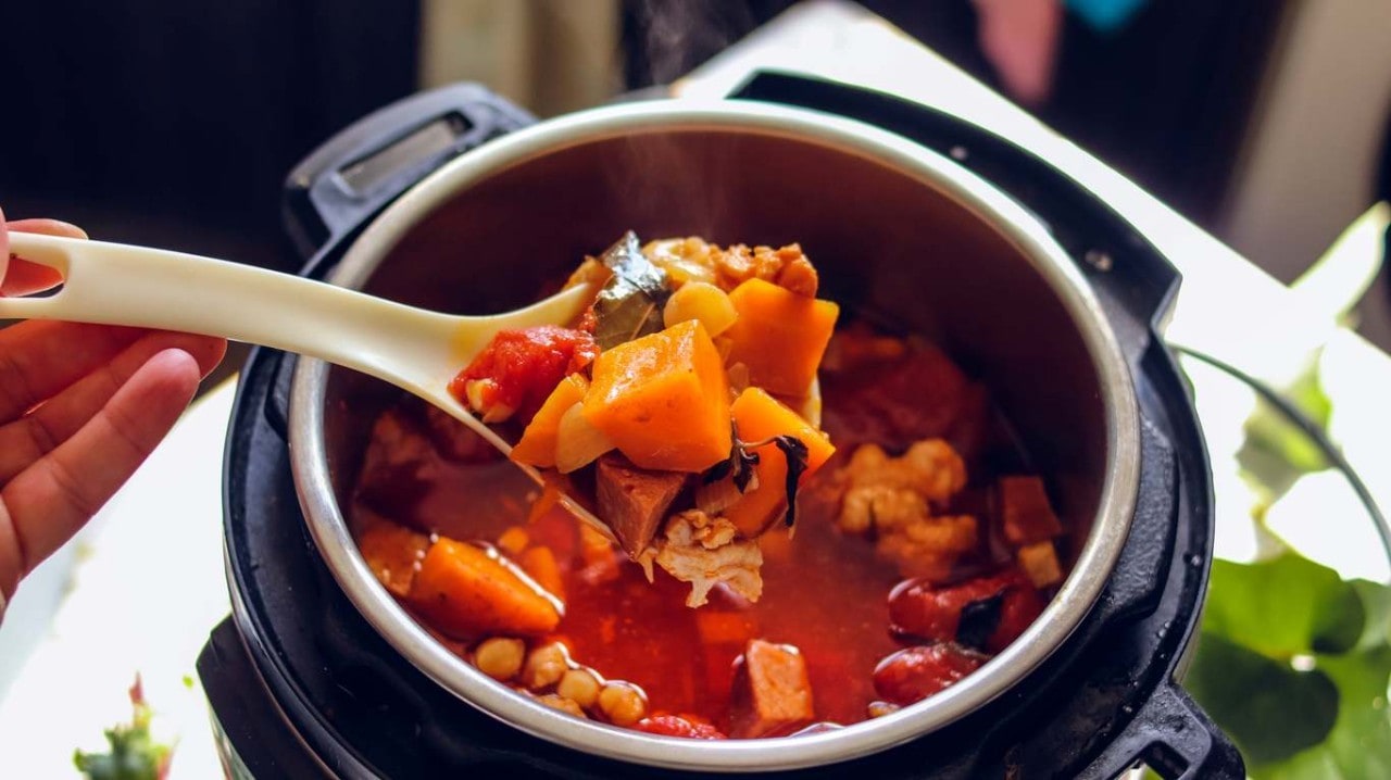 Panela elétrica contendo grãos e vegetais cozidos com pedaços de carne.
