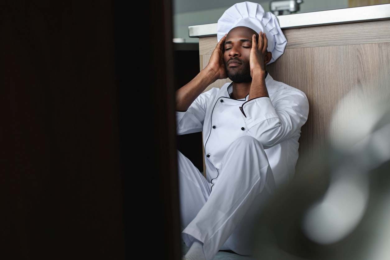 Chef sentado no chão da cozinha do seu restaurante