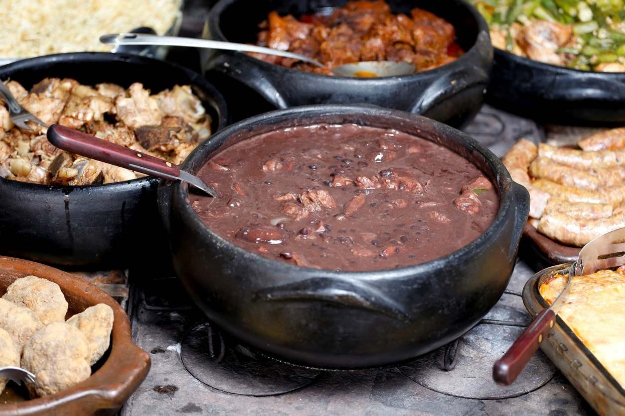 Feijoada completa servida em panelas de barro sobre fogão à lenha