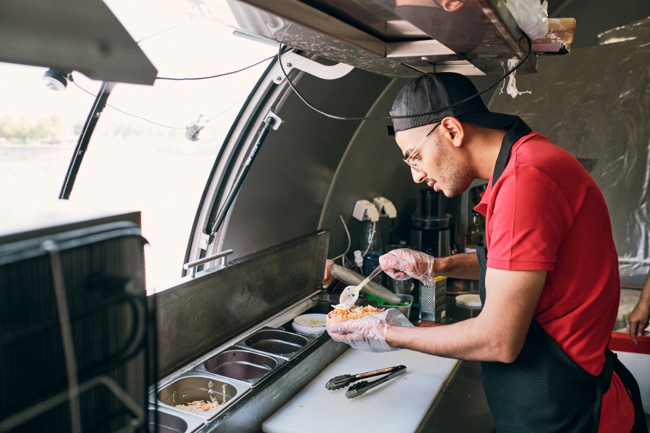 Homem preparando delicioso hotdog em seu food truck, com todo cuidado e atenção necessários. Homem preparando delicioso hotdog em seu food truck, com todo cuidado e atenção necessários.