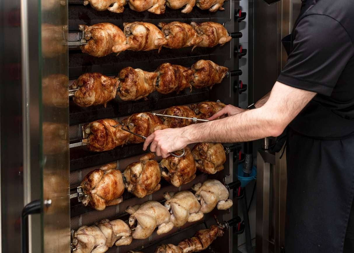 Cozinheiro checando o ponto dos frangos em sua máquina de assar frango