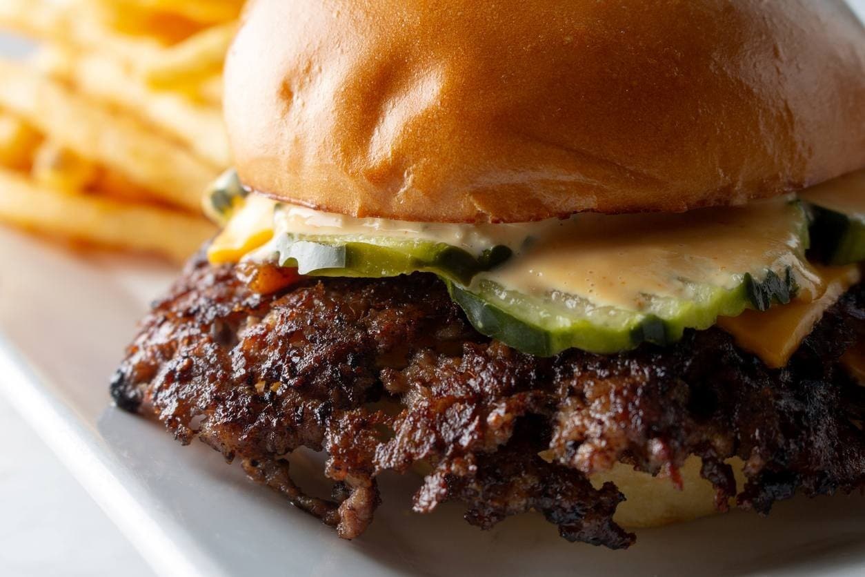 Foco em smash burguer artesanal, com fritas ao fundo do prato.