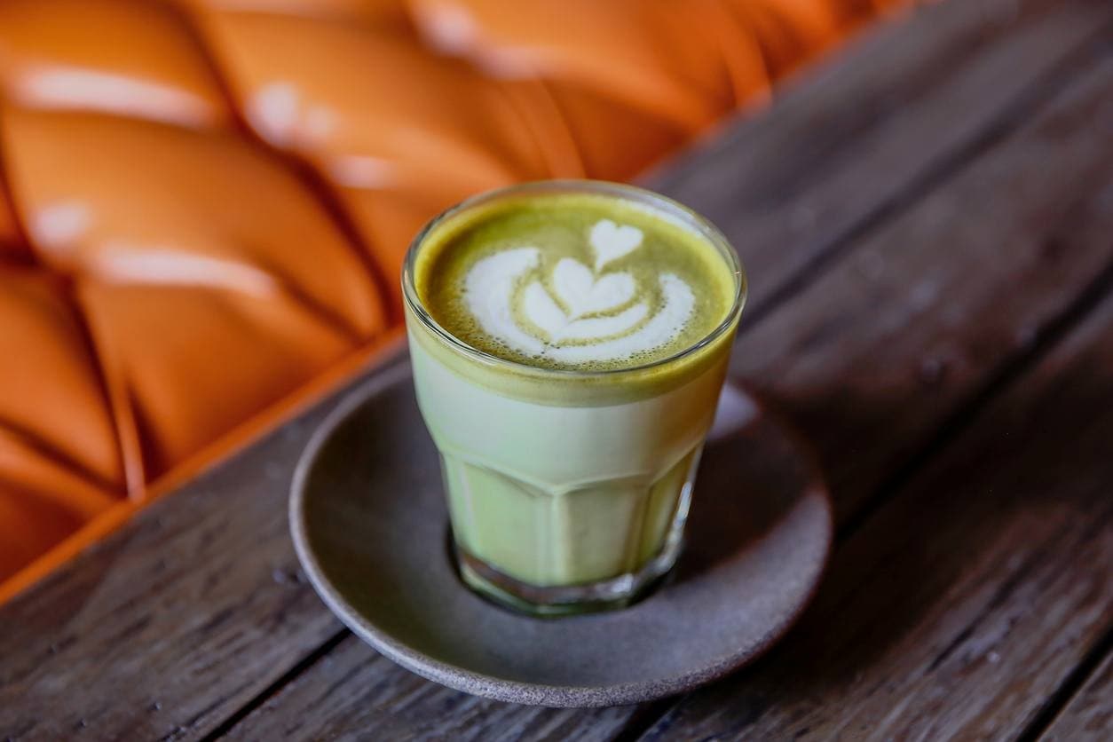 Matchá latte, servido em copo, com espuma de leite decorada.