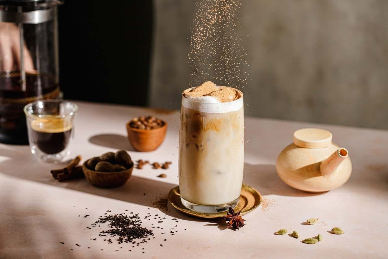 Café gelado cremoso com especiarias e espresso na mesa, sendo salpicado com chocolate em pó.