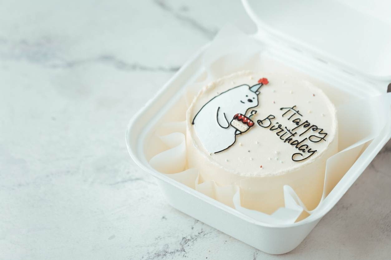 Bolo do tipo bentô cake, com urso fofo e engraçado, segurando um bolo festivo de aniversário.