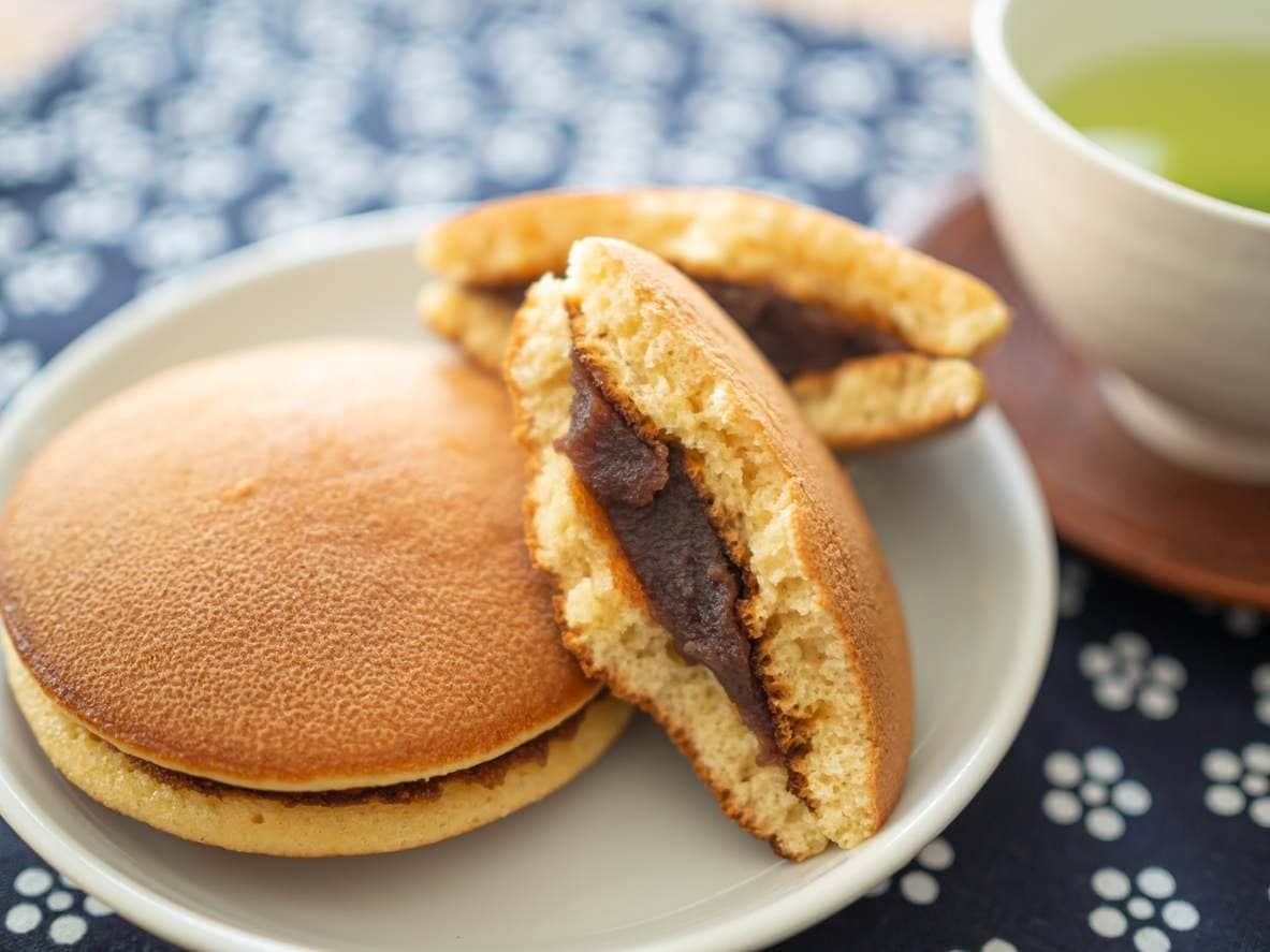 Um dorayaki cortado ao meio e um inteiro sobre pequeno prato, ao lado de xícara de chá verde.