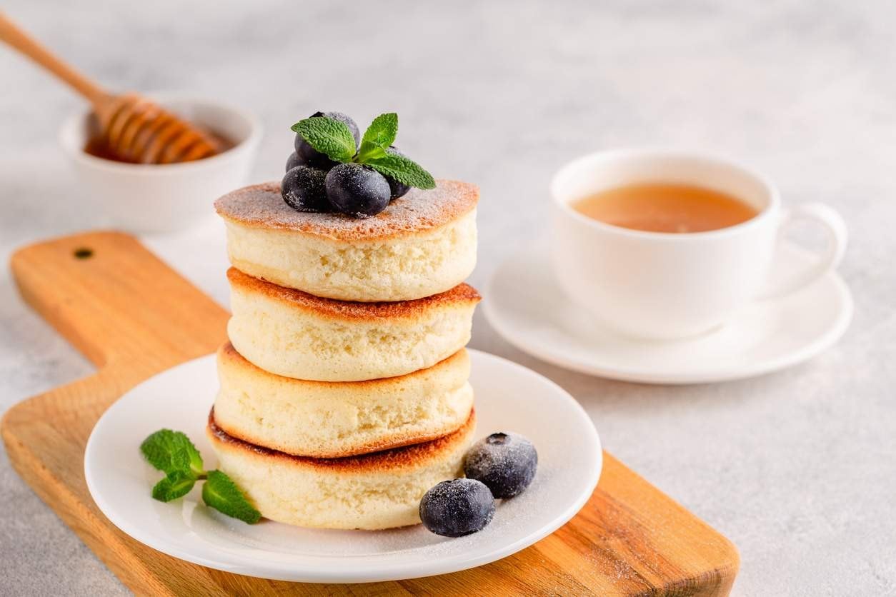 Quatro panquecas empilhadas, enfeitadas com blueberries e folhas de hortelã, polvilhada com açúcar de confeiteiro.