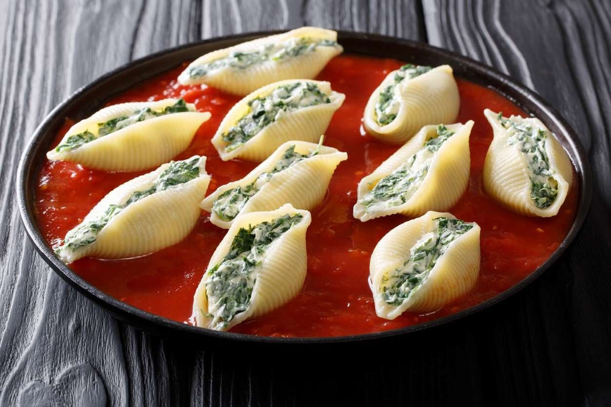 Porção de conchiglioni recheado de queijo e espinafre, servido ao molho sugo, antes de gratinar.