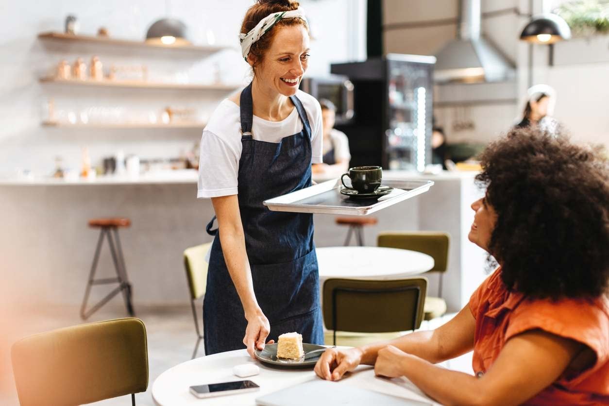 Garçonete simpática servindo bolo e café a uma mulher em uma cafeteria.