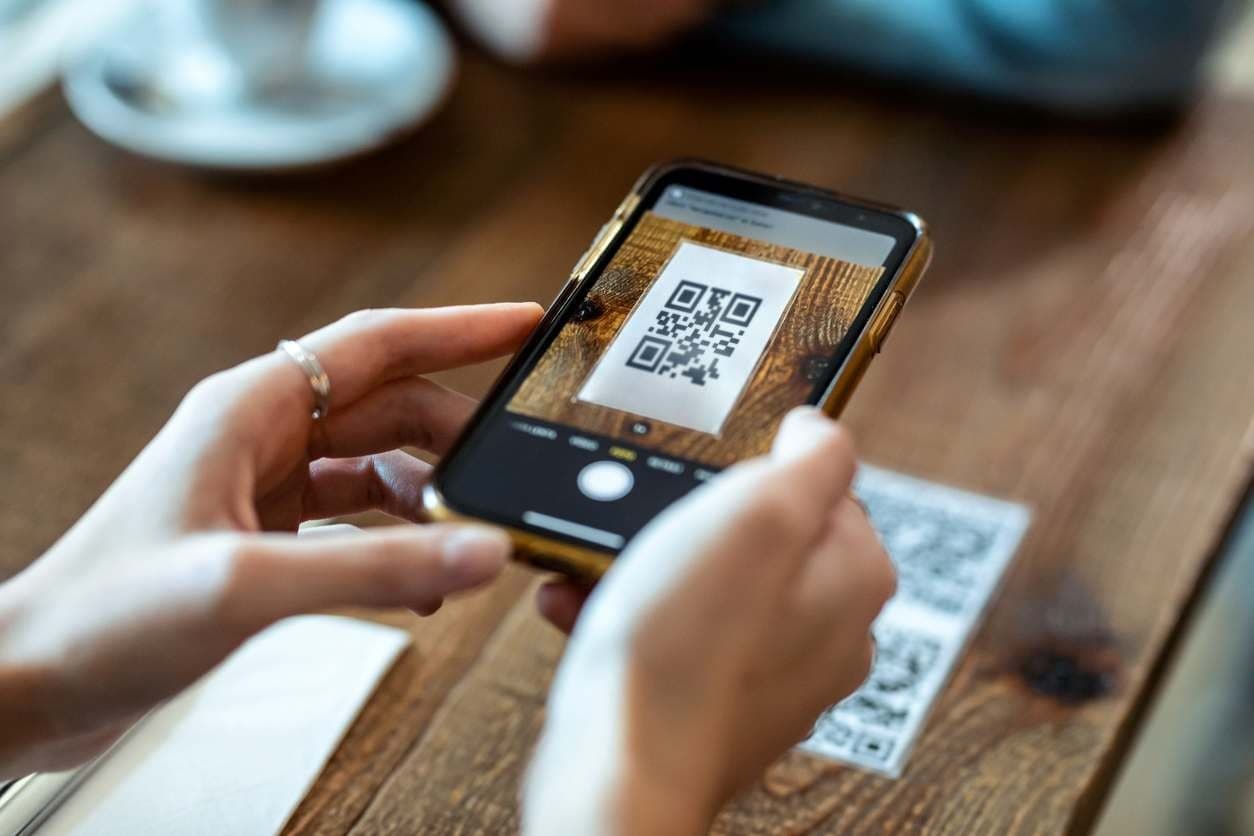 Mãos de jovem apontando o celular para um QR code de pesquisa de satisfação.