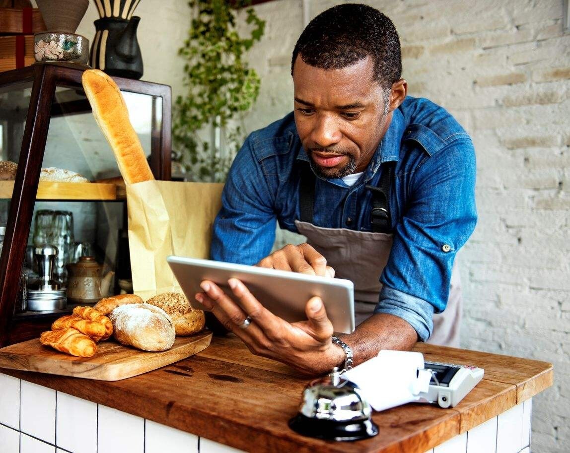 Homem com avental em uma padaria digitando em um tablet sobre o balcão. Homem com avental em uma padaria digitando em um tablet sobre o balcão.