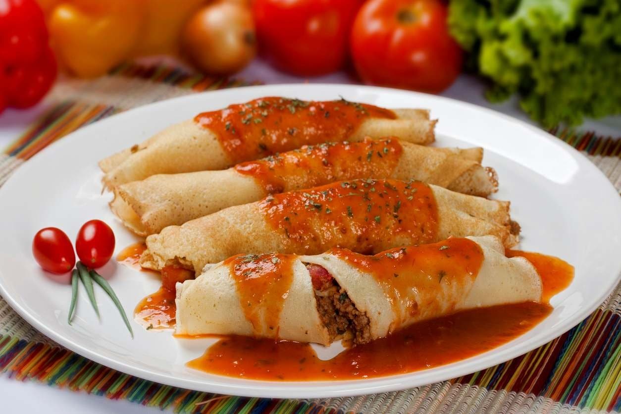 Quatro panquecas de carne moída muito bem empratadas, cobertas com molho de tomate.
