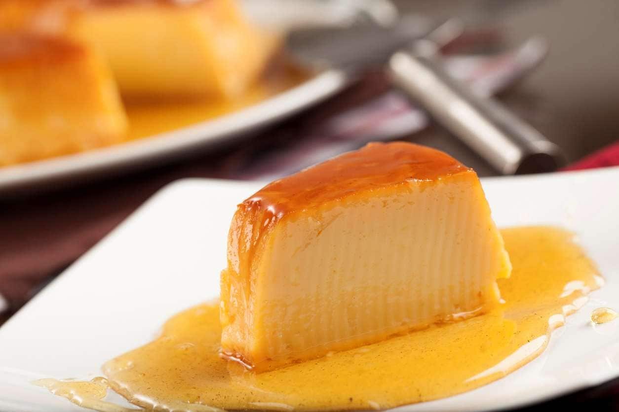Pedaço de pudim de leite condensado com calda de caramelho servido em prato branco