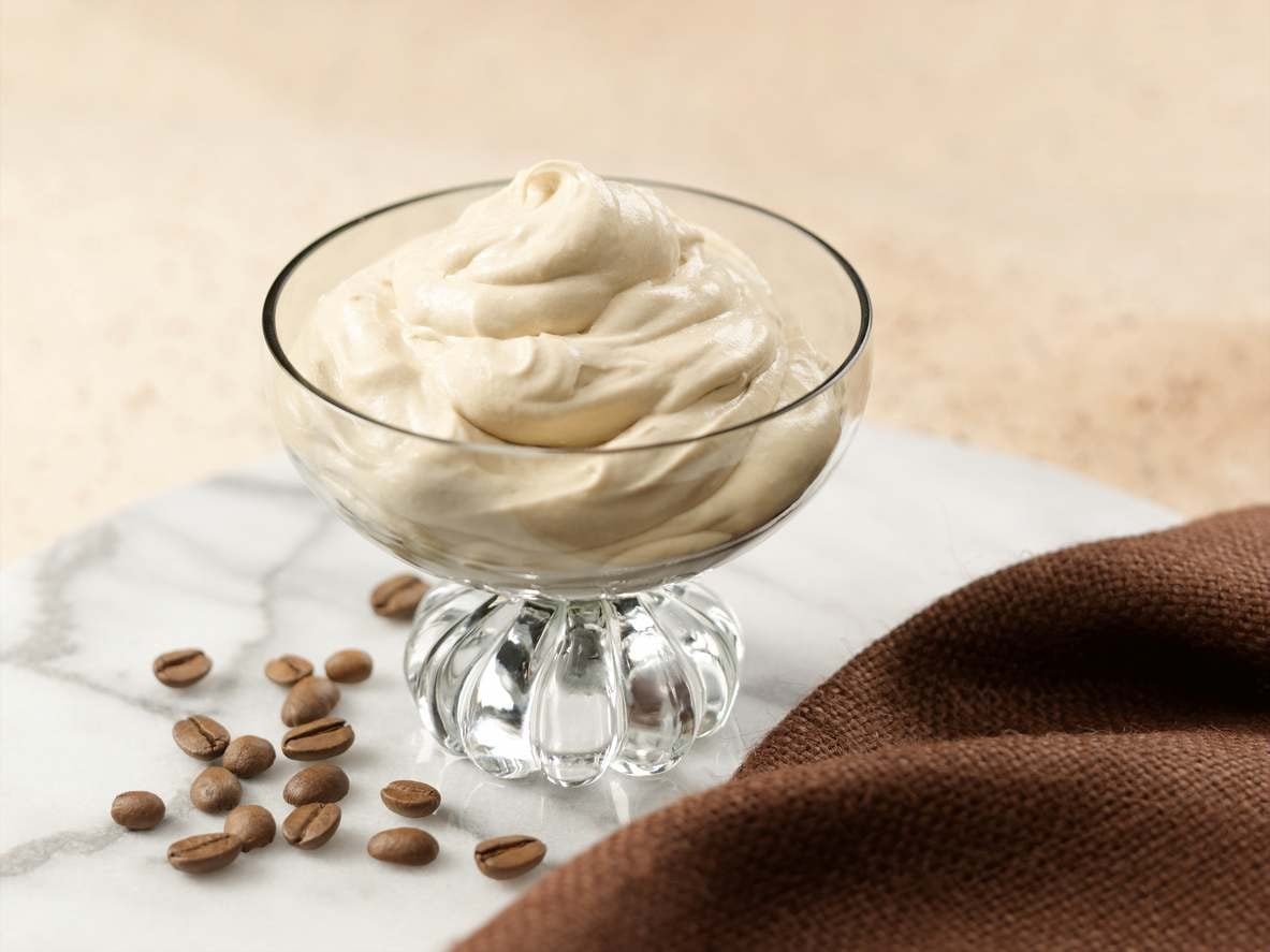 Mousse de café em taça de vidro com grãos de café espalhados sobre superfície de mármore.