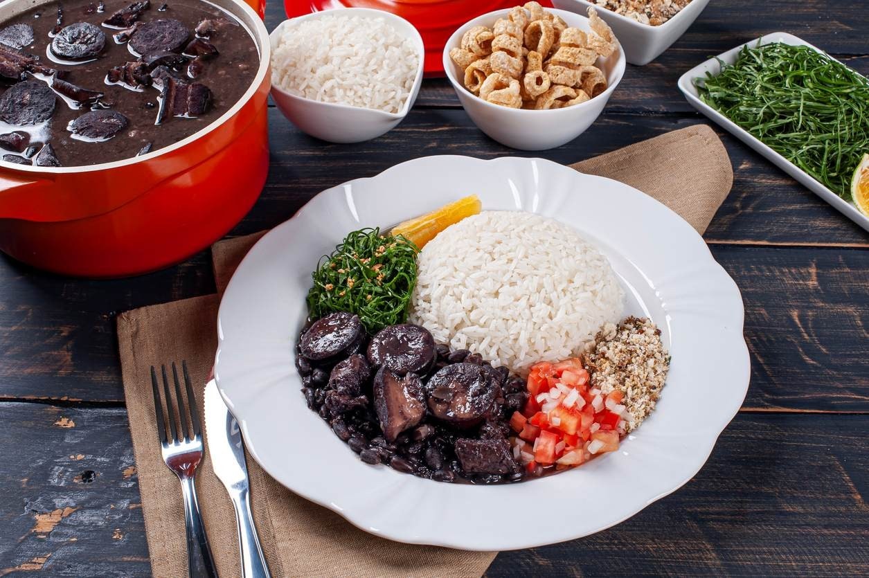 Prato de feijoada completa com arroz, couve e farofa ao lado da panela, representando a culinária brasileira como foco do marketing para restaurantes.