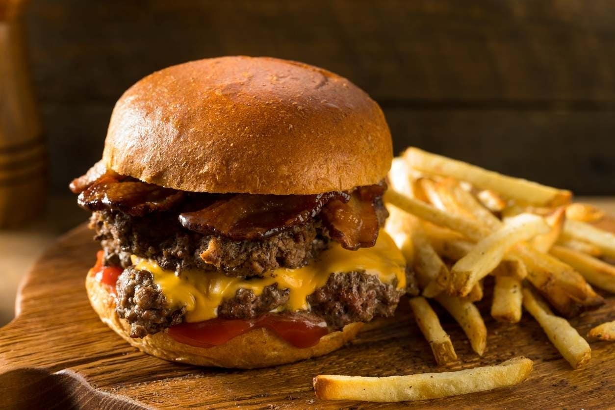 Smash burguer com bacon, queijo e duas carnes, ao lado de batatas fritas.