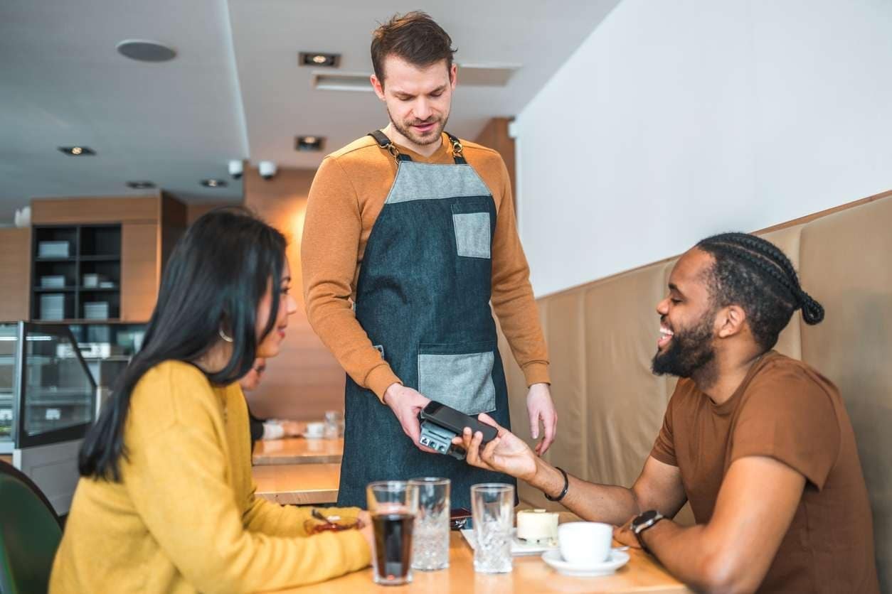 Casal pagando uma conta em cafeteria usando um celular, com taxa de serviço
