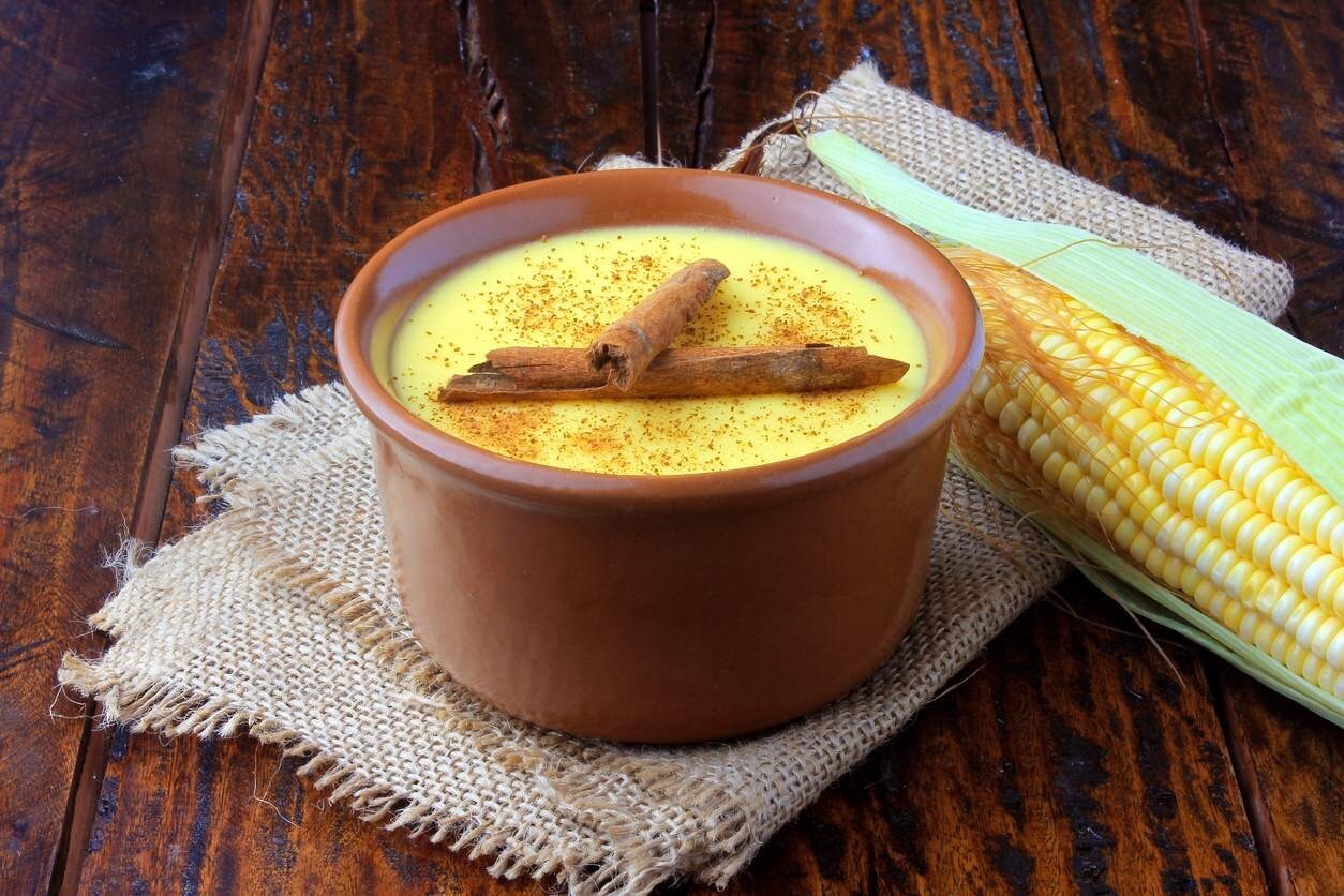 Cumbuca de curau de milho decorado com pó e pau de canela. Ao lado, uma espiga. Cumbuca de curau de milho decorado com pó e pau de canela. Ao lado, uma espiga.
