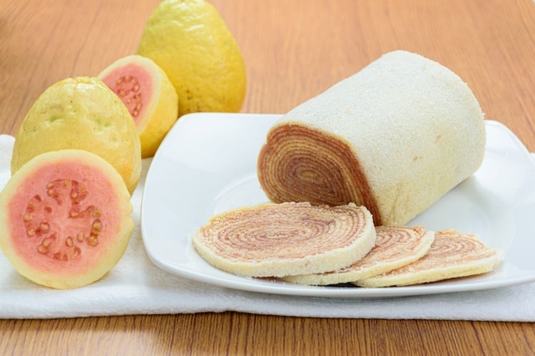 Bolo de rolo fatiado acompanhado de goiabas frescas em um prato branco. Bolo de rolo fatiado acompanhado de goiabas frescas em um prato branco.