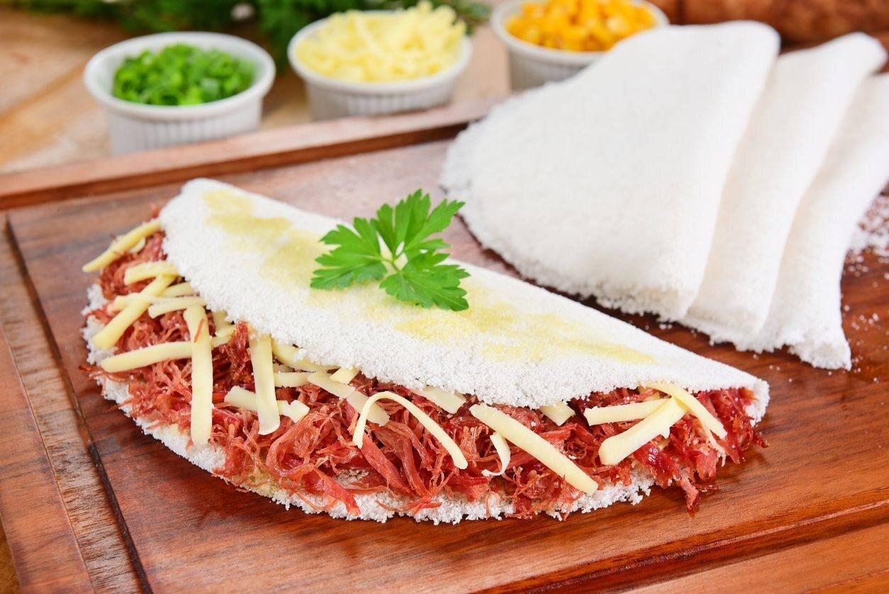 Tapioca recheada com carne seca desfiada e queijo sobre tábua de madeira Tapioca recheada com carne seca desfiada e queijo sobre tábua de madeira