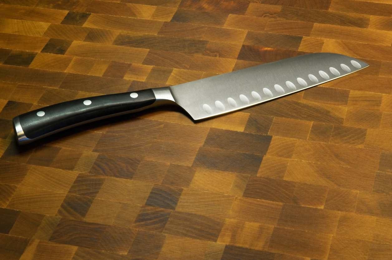Faca santoku com lâmina larga e alvéolos sobre tábua de madeira, destacando o formato característico desse modelo japonês.