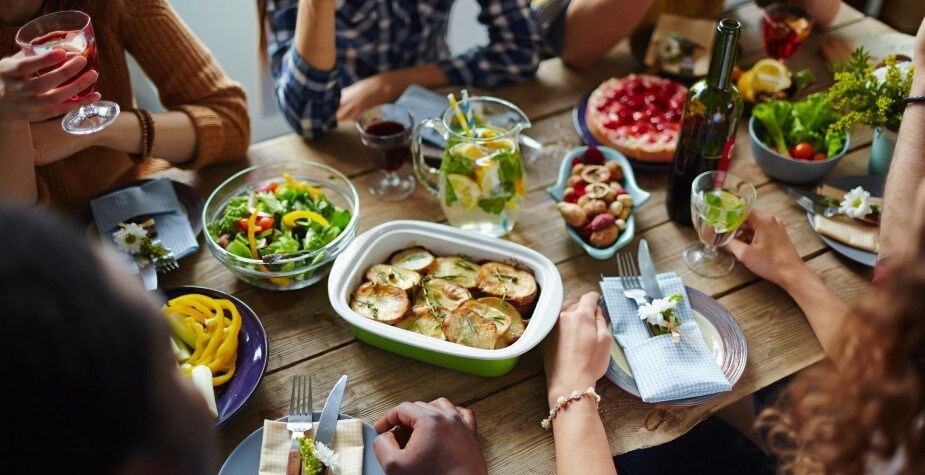 Grupo de pessoas reunidos em volta da mesa enquanto compartilham pratos vegetarianos em food service Grupo de pessoas reunidos em volta da mesa enquanto compartilham pratos vegetarianos em food service