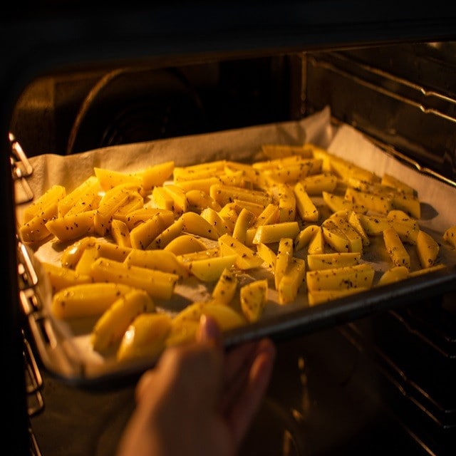 Forma no forno, coberta com papel manteiga. Sobre ela, palitos de batata temperada para assar. Forma no forno, coberta com papel manteiga. Sobre ela, palitos de batata temperada para assar.