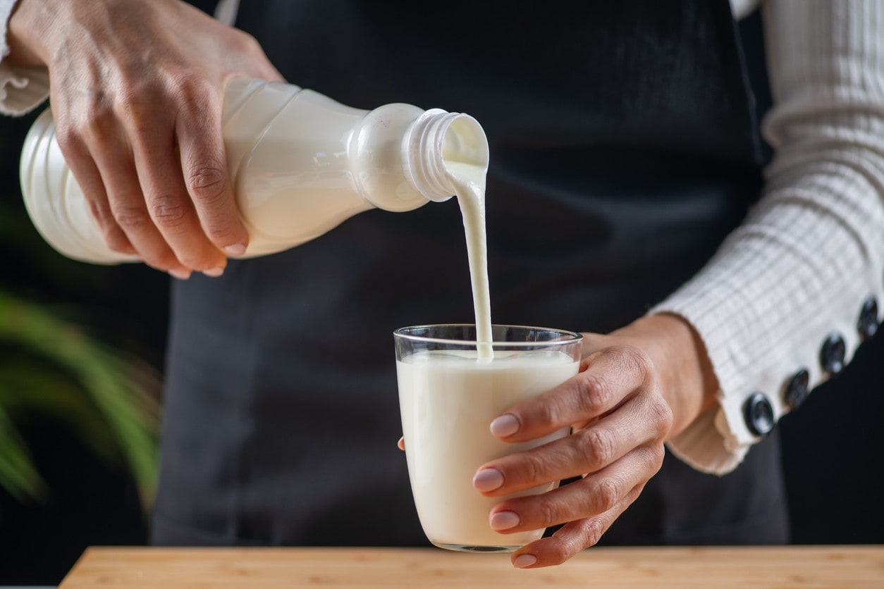 Pessoa de avental servindo kefir da garrafa direto em um copo de vidro. Pessoa de avental servindo kefir da garrafa direto em um copo de vidro.