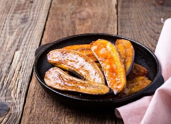 Panela de ferro com barquinhas de banana caramelizada, sobre mesa de madeira Panela de ferro com barquinhas de banana caramelizada, sobre mesa de madeira