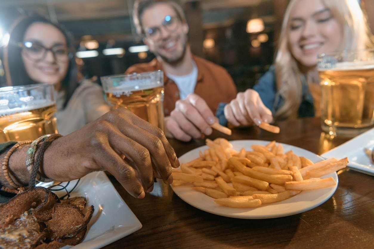 Amigos compartilham porção de batatas fritas e cerveja em bar, representando um combo de finger food com bebidas.