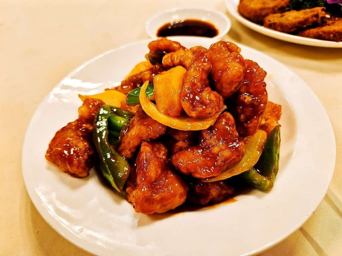 Prato bem servido de porco agridoce, com cebola, pimentão e bastante molho.