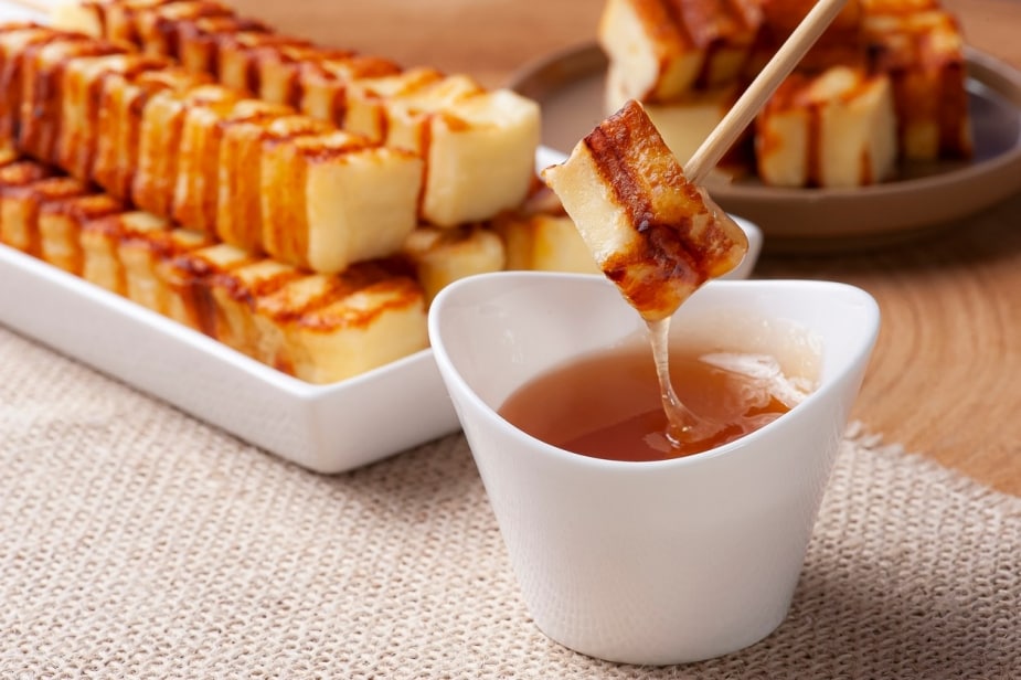 Porções de queijo coalho grelhado inteiras e em cubinhos. Detalhe para um pedaço que está sendo mergulhado em molho à base de mel. Porções de queijo coalho grelhado inteiras e em cubinhos. Detalhe para um pedaço que está sendo mergulhado em molho à base de mel.