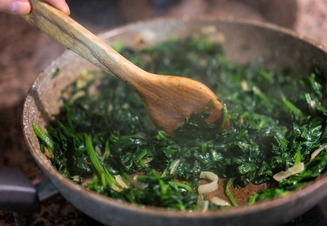 Detalhe de frigideira refogando espinafre com alho e cebola.