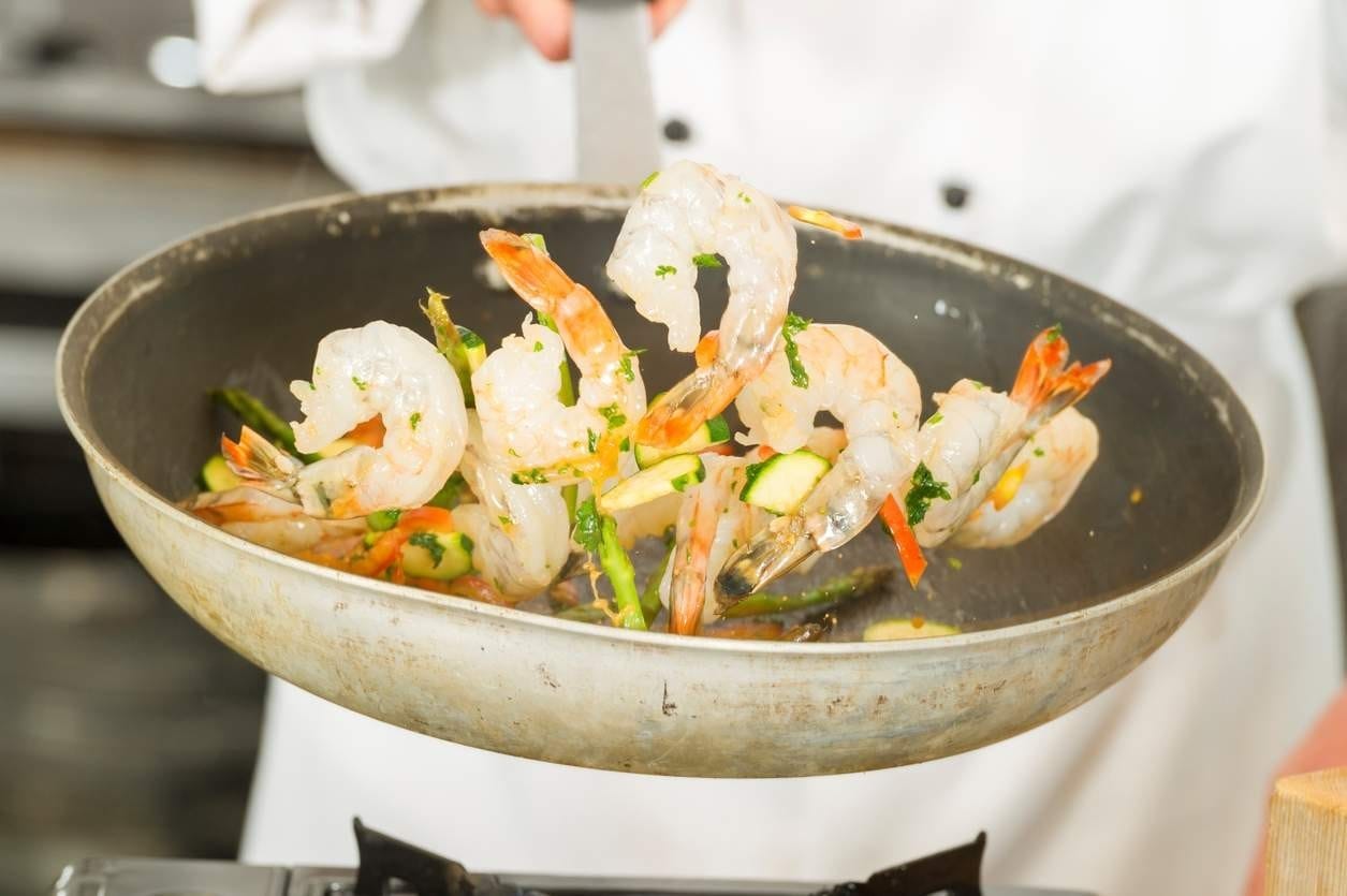 Chef está salteando camarões - na frigideira, com alguns camarões no ar.