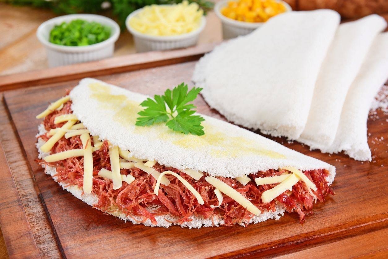 Tapioca recheada com carne seca desfiada e queijo sobre tábua de madeira Tapioca recheada com carne seca desfiada e queijo sobre tábua de madeira
